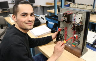 Mechatronics student smiles for the camera while he works on a project