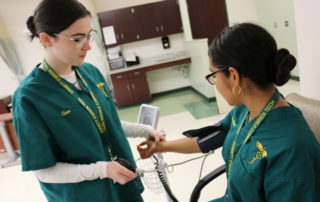 Two Health Technology students practice measuring blood pressure on each other