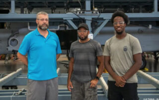 Sikorsky intern Tahjay Greene, right, with mentors Travis White, left, and Jerry Carrasquillo, center, stand in front of a CH-53K heavy-lift cargo helicopter in production at Sikorsky Aircraft's manufacturing plant in Stratford, CT